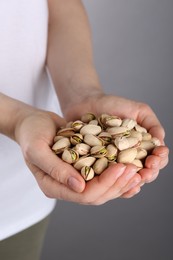 Photo of Woman holding handful of tasty pistachios on grey background, closeup