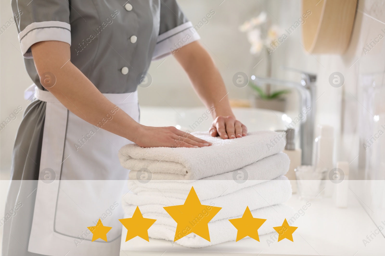 Image of Five Star Luxury Hotel. Young chambermaid with stack of fresh towels in bathroom, closeup