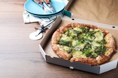 Photo of Delicious pizza with pesto, cheese and arugula in cardboard box served on wooden table