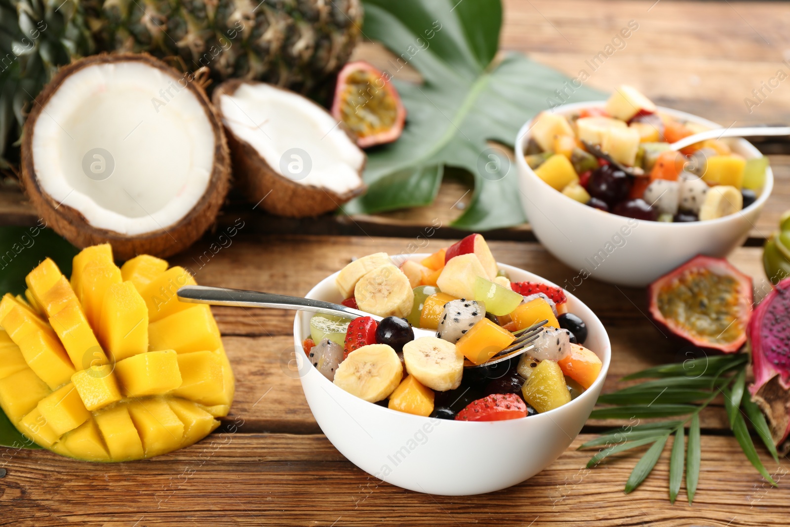 Photo of Delicious exotic fruit salad and ingredients on wooden table