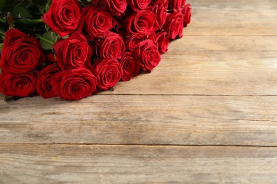 Photo of Luxury bouquet of fresh red roses on wooden table, space for text