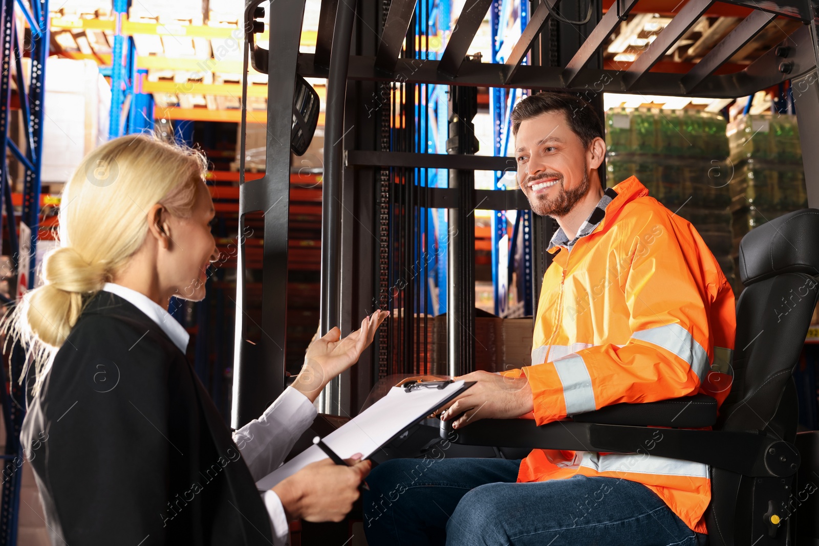 Photo of Happy worker talking with manager while sitting in forklift truck at warehouse