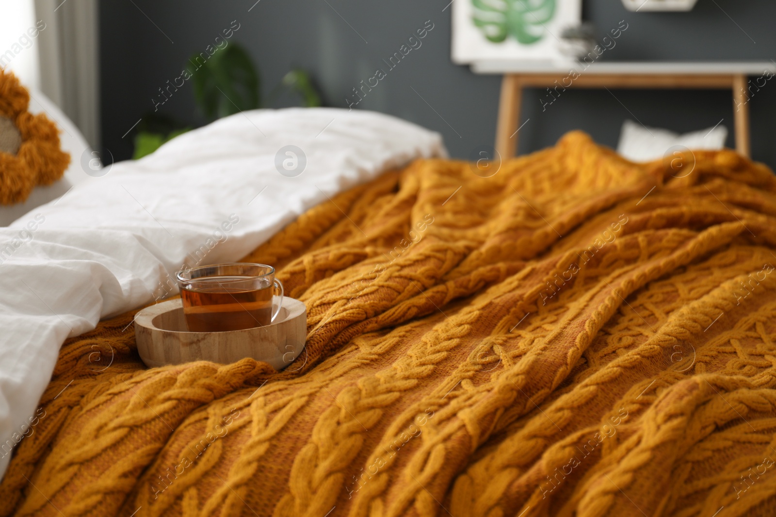 Photo of Cup of tea and knitted orange plaid on bed indoors, closeup