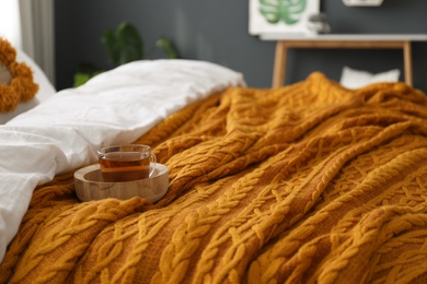 Cup of tea and knitted orange plaid on bed indoors, closeup