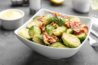 Photo of Delicious cooked Brussels sprouts with bacon served on grey table, closeup