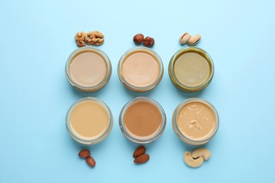 Different types of delicious nut butters and ingredients on light blue background, flat lay