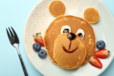 Creative serving for kids. Plate with cute bear made of pancakes and berries on light blue table, flat lay