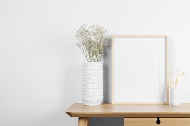 Photo of Empty photo frame, vases with dry decorative spikes and gypsophila flowers on wooden table. Mockup for design