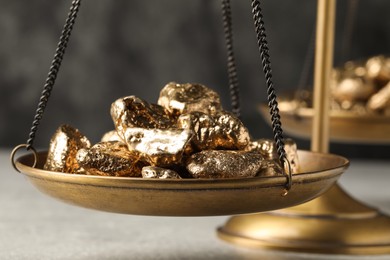 Photo of Vintage scales with gold nuggets on light table against grey background, closeup