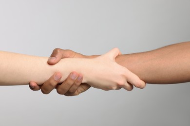 Photo of International relationships. People holding hands on light grey background, closeup