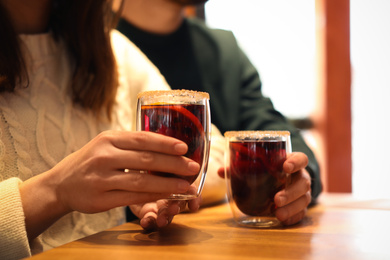 Photo of Lovely couple with tasty mulled wine at table in cafe, closeup