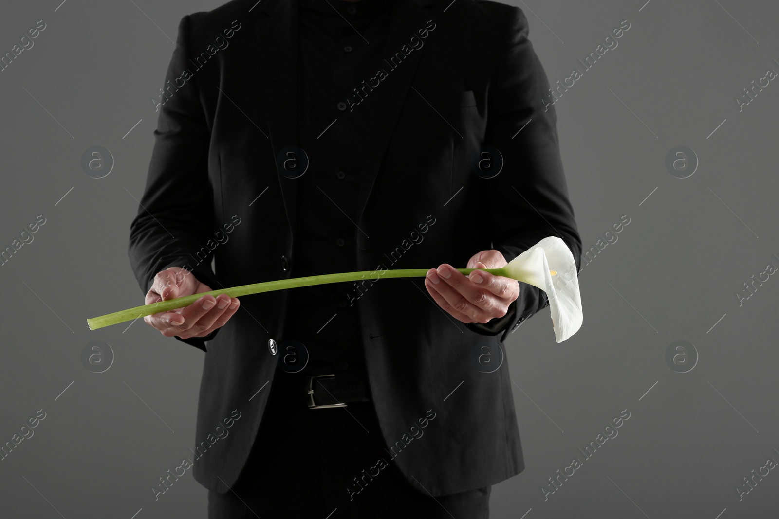 Photo of Man with calla lily flower on grey background, closeup. Funeral ceremony