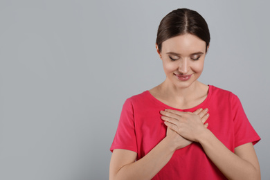 Photo of Beautiful grateful woman with hands on chest against light grey background. Space for text