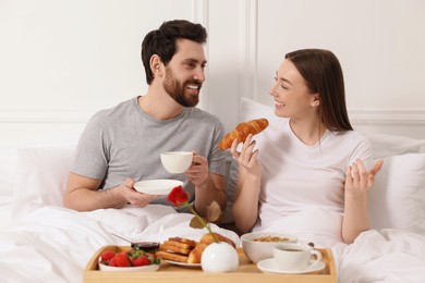 Happy couple having tasty breakfast in bed at home
