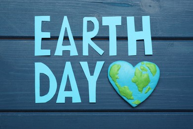 Photo of Words Earth Day and heart shaped plasticine planet on blue wooden table, flat lay