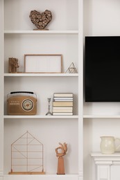 Photo of Stylish shelves with different decor elements and TV set in room. Interior design