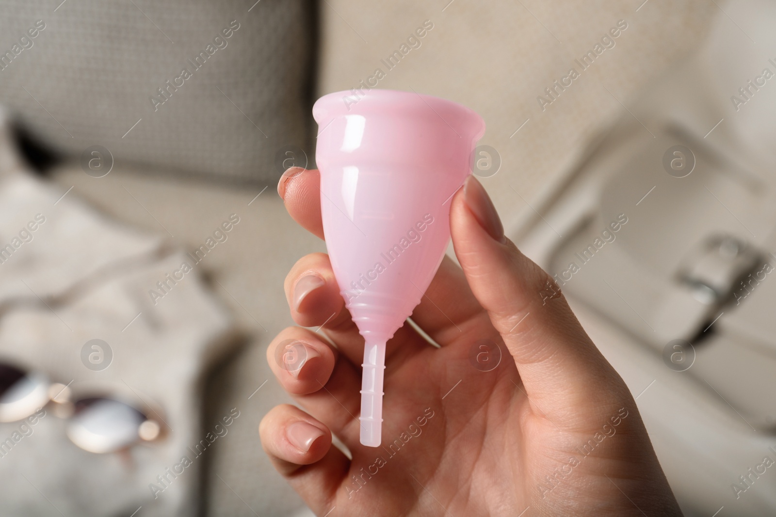 Photo of Woman holding pink menstrual cup on blurred background, closeup