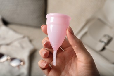 Woman holding pink menstrual cup on blurred background, closeup