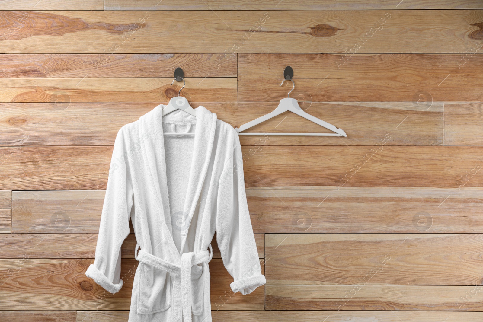 Photo of Soft comfortable bathrobe hanging on wooden wall, space for text