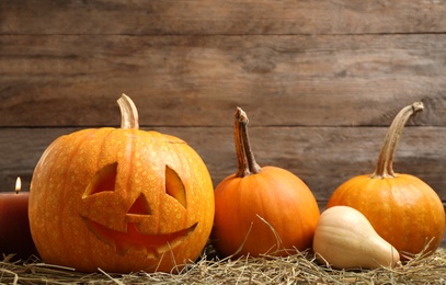 Photo of Spooky Jack pumpkin head lantern on hay against wooden background. Halloween decoration