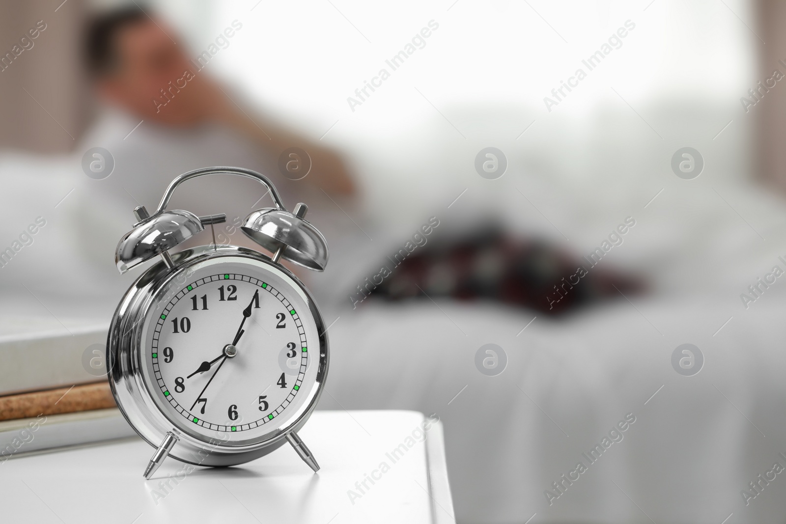 Photo of Man waking up in bedroom, focus on alarm clock. Space for text