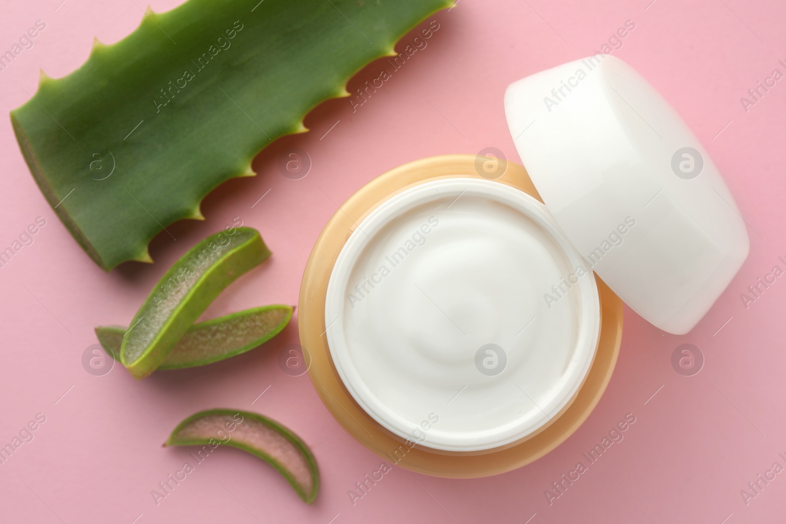 Photo of Jar with cream and cut aloe leaf on pink background, flat lay