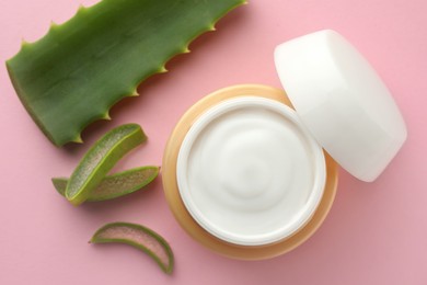 Jar with cream and cut aloe leaf on pink background, flat lay
