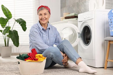 Happy housewife with laundry basket near washing machine at home