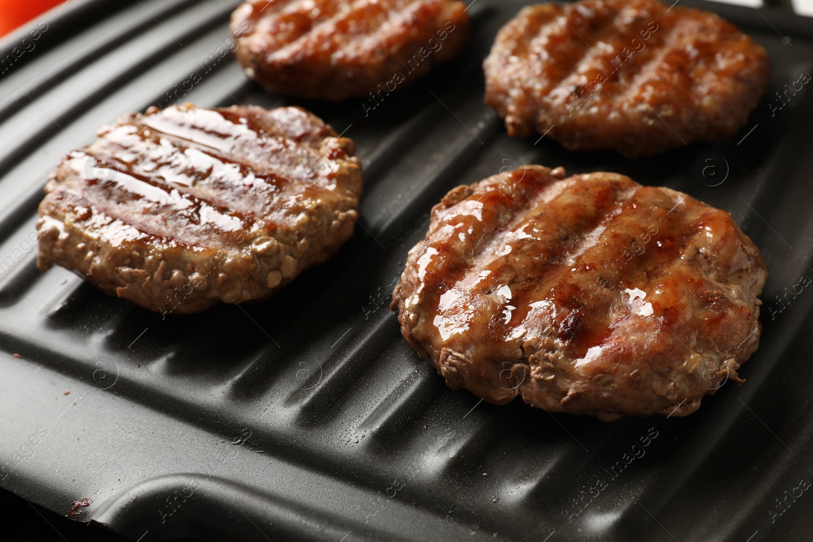 Photo of Delicious hamburger patties cooking on electric grill, closeup