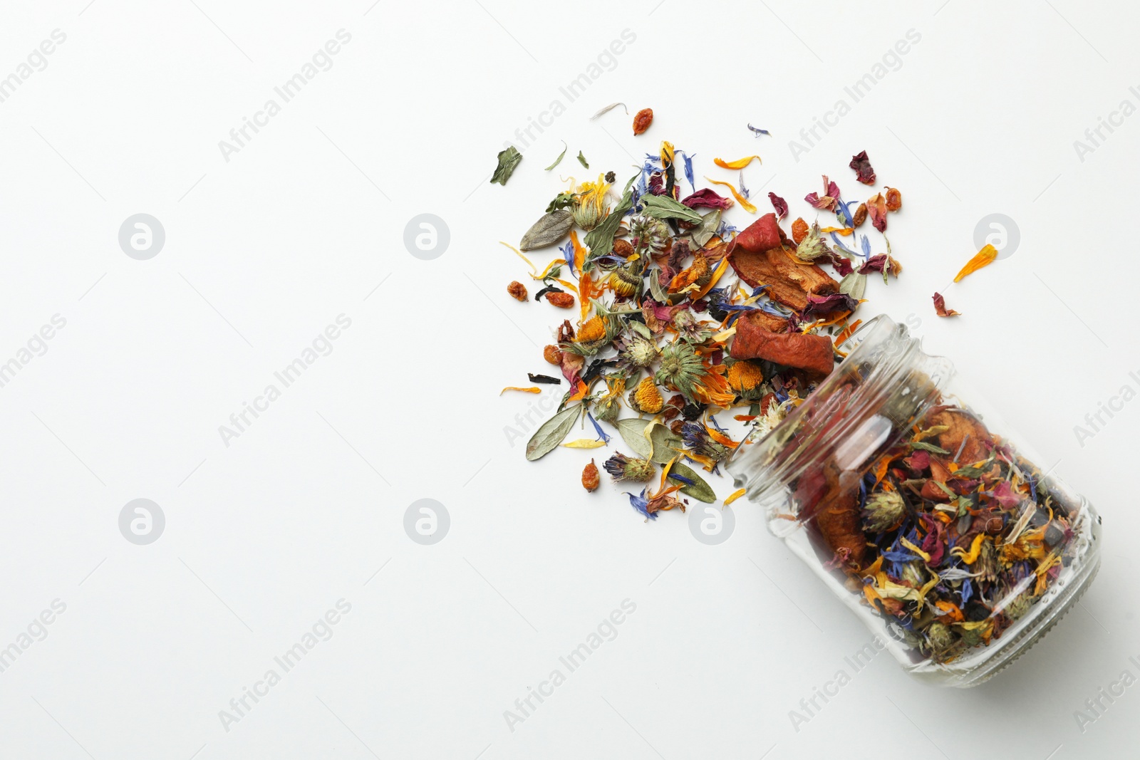 Photo of Overturned glass jar with dry herbal tea on white background, top view. Space for text