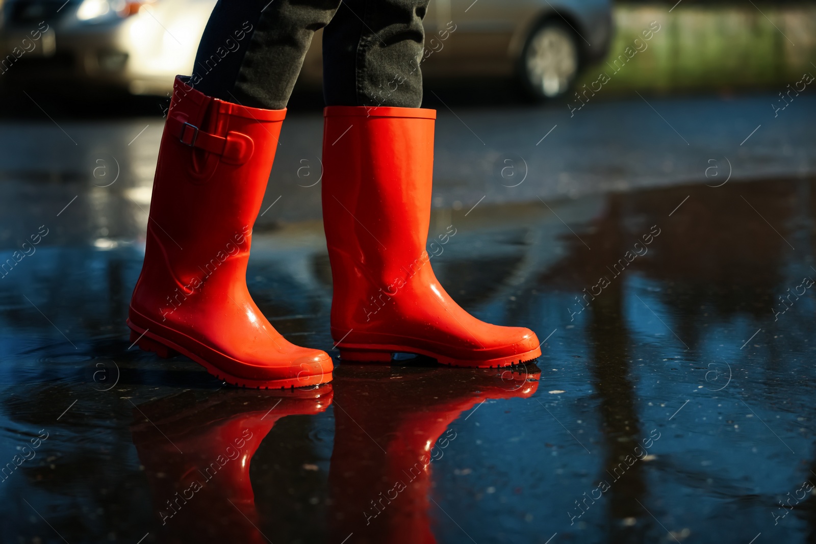 Photo of Woman with red rubber boots walking in puddle, closeup. Rainy weather