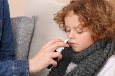 Photo of Mother using nasal spray to treat her little son on sofa, closeup