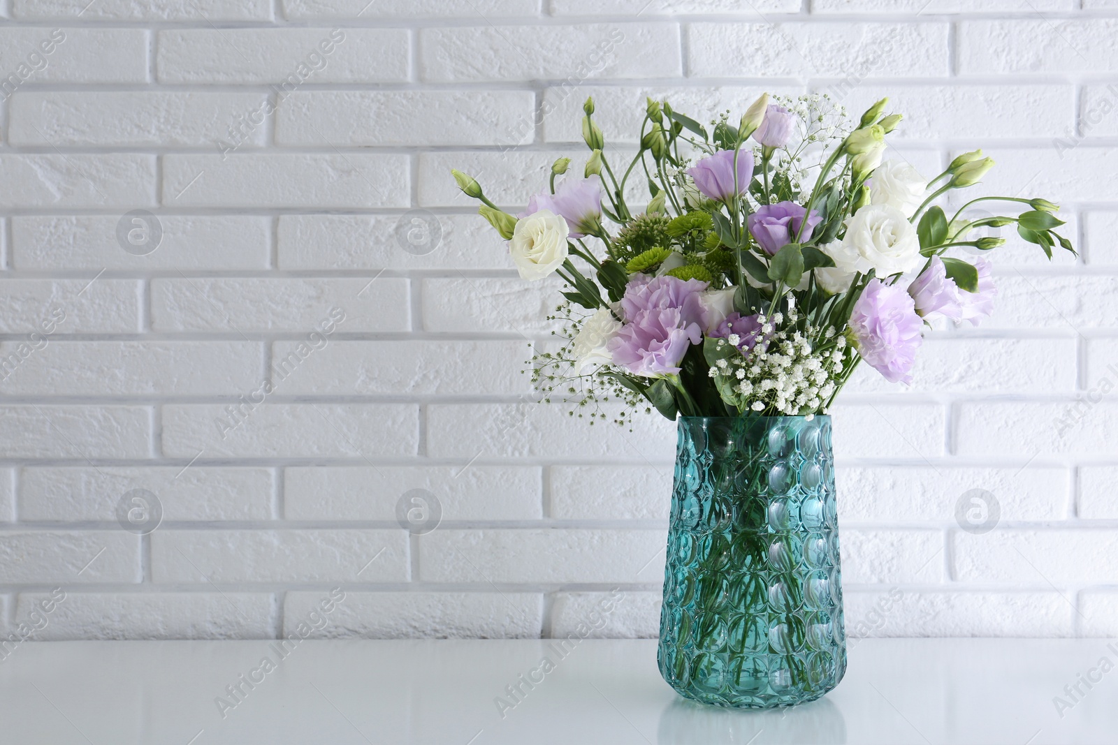 Photo of Bouquet of beautiful Eustoma flowers on table near white brick wall. Space for text