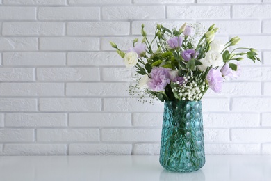 Bouquet of beautiful Eustoma flowers on table near white brick wall. Space for text