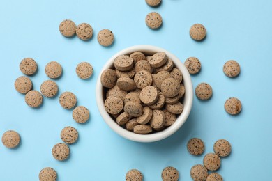 Vitamin pills in bowl on light blue background, top view