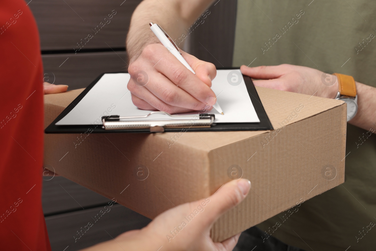 Photo of Man signing for delivered parcel from courier indoors, closeup