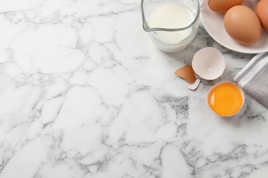 Raw chicken eggs, shell with yolk and jug of milk on white marble table, flat lay. Space for text