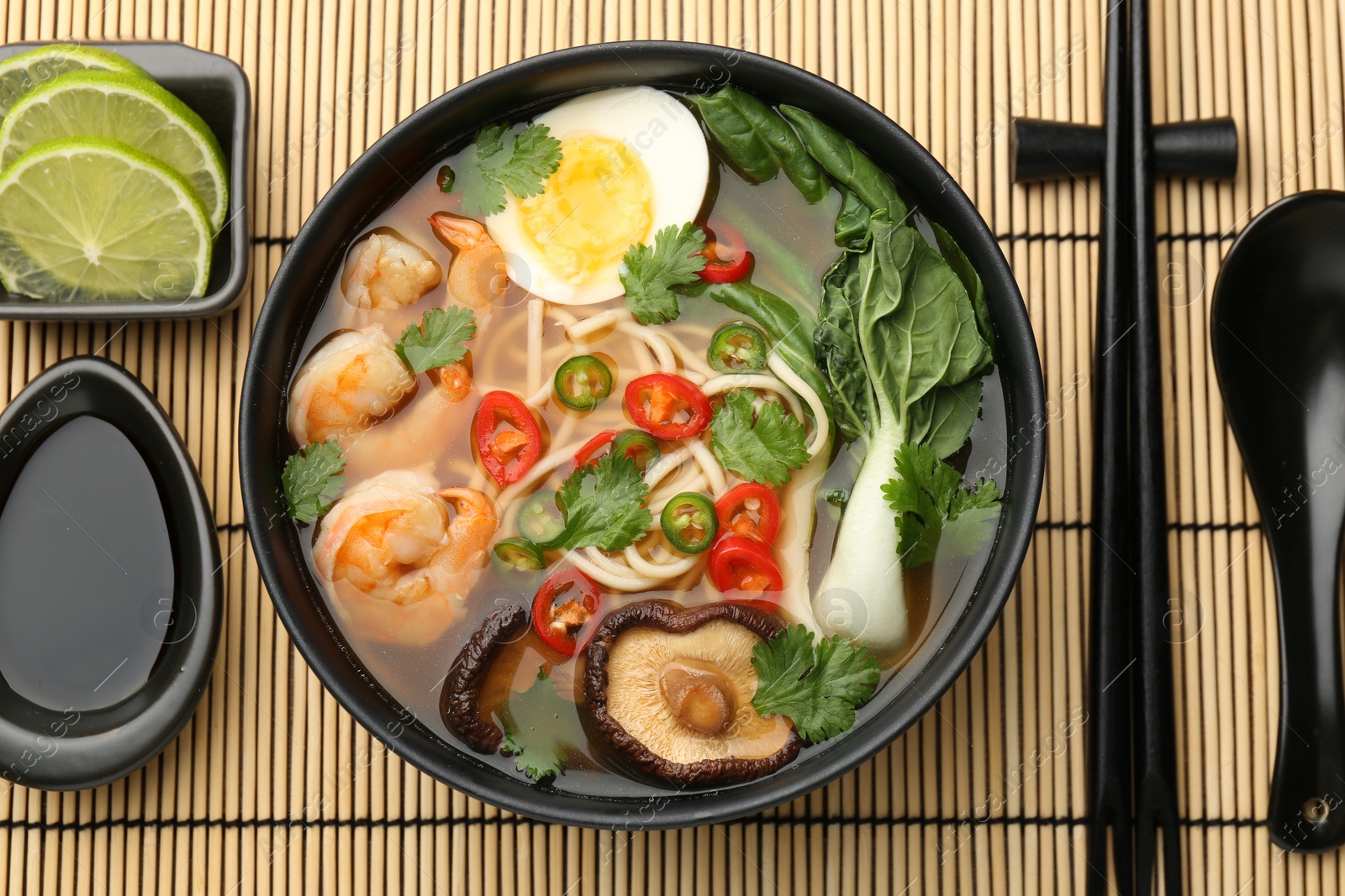 Photo of Delicious ramen with shrimps and egg in bowl served on bamboo mat, flat lay