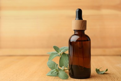 Bottle of mint essential oil and fresh herb on wooden table, space for text