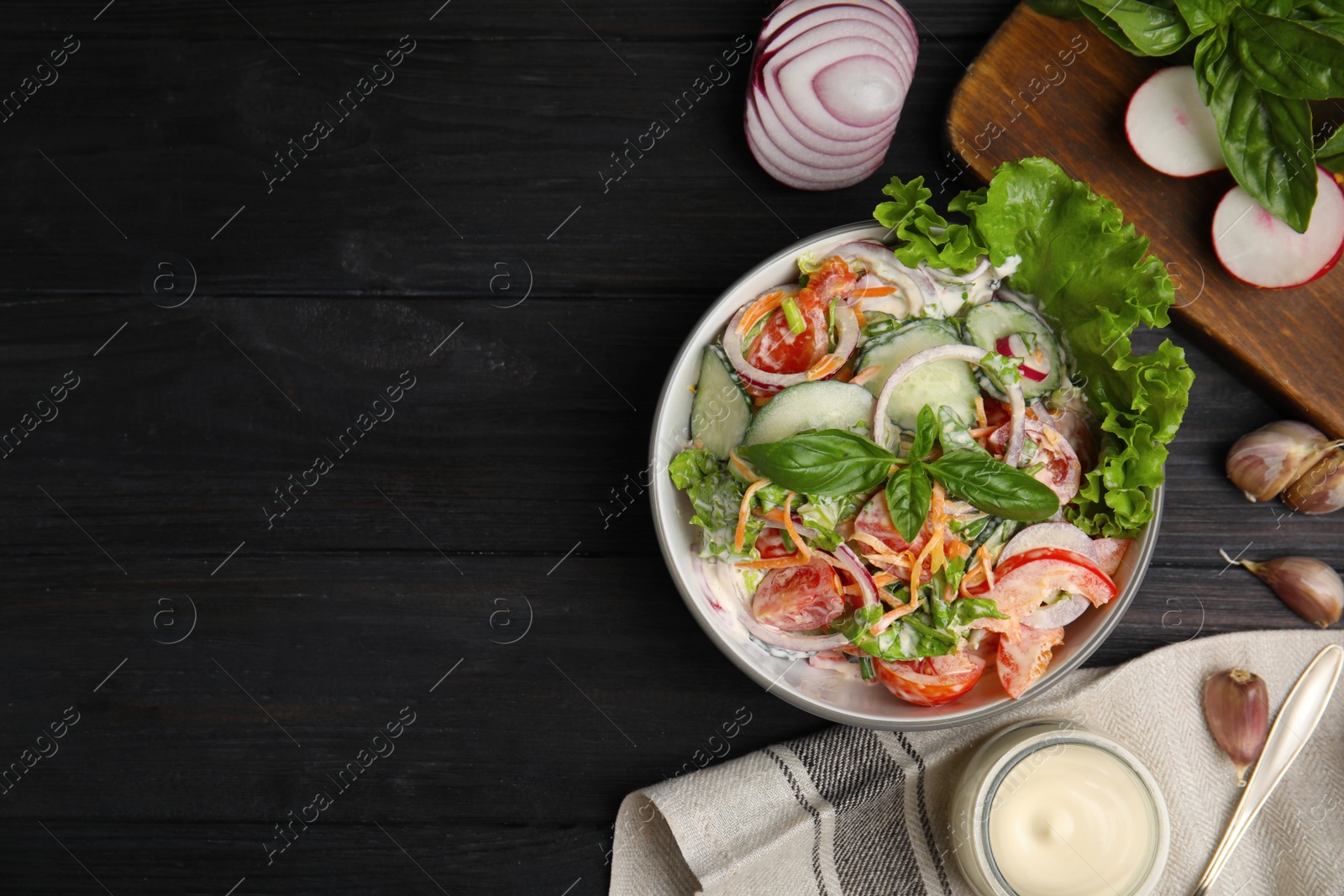 Photo of Bowl of delicious vegetable salad dressed with mayonnaise and ingredients on black wooden table, flat lay. Space for text