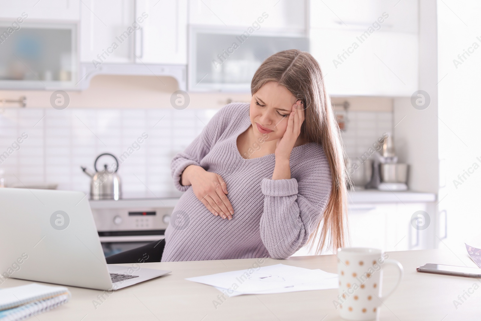 Photo of Young pregnant woman suffering from headache in home office