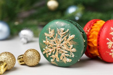 Photo of Different decorated Christmas macarons and festive decor on white table, closeup