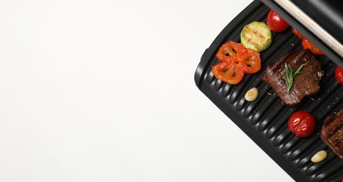 Photo of Electric grill with tasty meat, spices and vegetables on white table, top view. Space for text