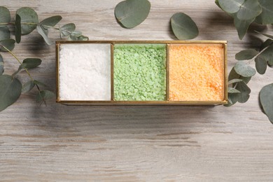 Photo of Different types of sea salt and eucalyptus branches on wooden table, flat lay. Space for text