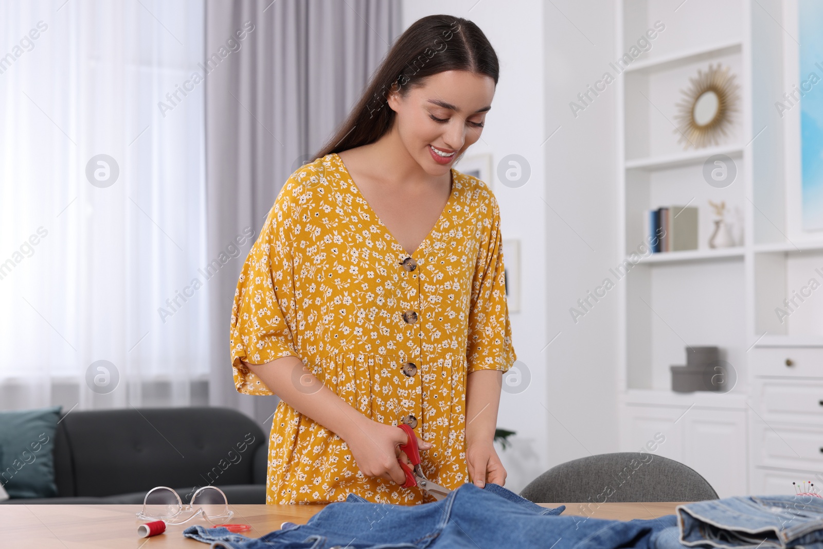 Photo of Happy woman cutting hem of jeans at table indoors