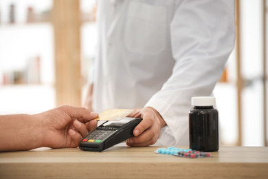 Photo of Customer using terminal for contactless payment with credit card in pharmacy, closeup