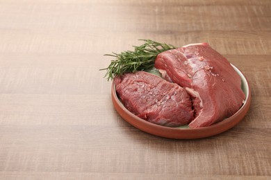 Photo of Pieces of raw beef meat with spices and rosemary on wooden table, space for text