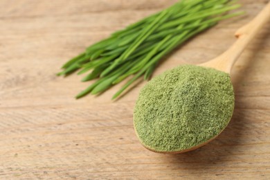 Wheat grass powder in spoon on wooden table, closeup. Space for text