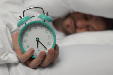 Sleepy man with alarm clock in bed at home, selective focus. Space for text