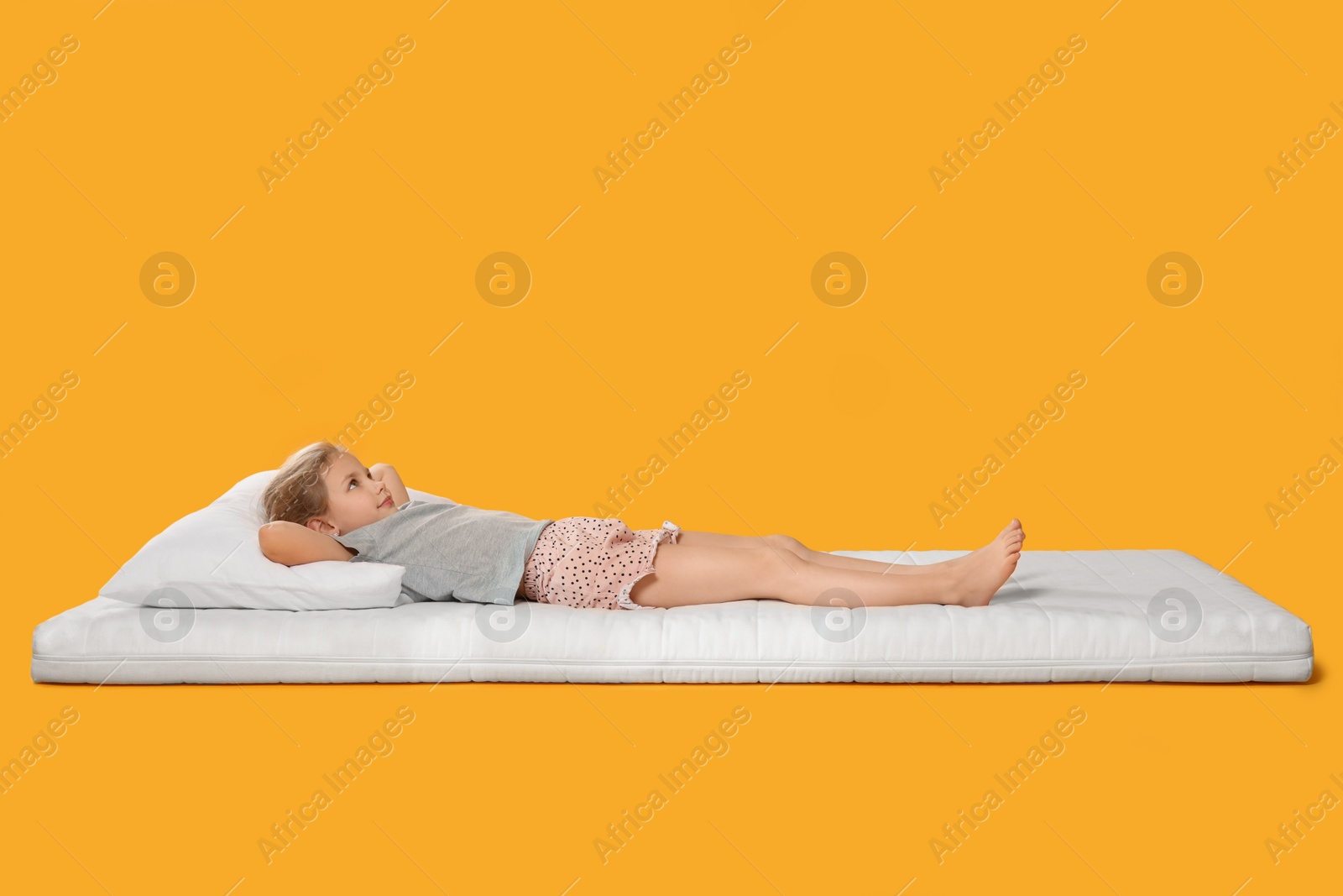 Photo of Little girl lying on comfortable mattress against orange background, space for text